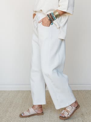 A cropped mid-shot of wide-leg barrel sweatpants in bone white, styled with a cream top, buckle sandals, and a stacked mix of beaded bracelets and a gold cuff — the kind of effortless, put-together comfort that makes you want to run errands and look