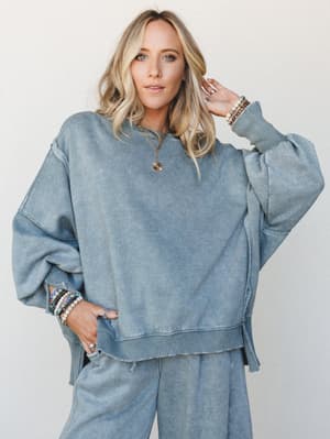 An oversized acid-wash sweatshirt in a muted blue-grey paired with matching wide-leg sweatpants — the kind of set that looks like you tried just enough, layered with stacked bracelets and a gold pendant necklace for that effortless everyday feel.