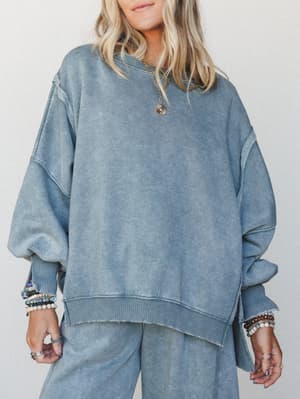 An oversized acid-wash sweatshirt in a muted slate blue layered with stacked beaded bracelets and a gold chain necklace — the kind of effortless set that looks like you tried just enough.