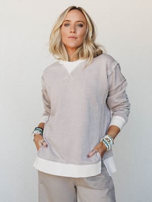 A relaxed, lived-in oversized crewneck sweatshirt in muted ash mocha layered over a white tee, styled with wide-leg pants and stacked beaded bracelets — the kind of outfit that looks effortless without trying.