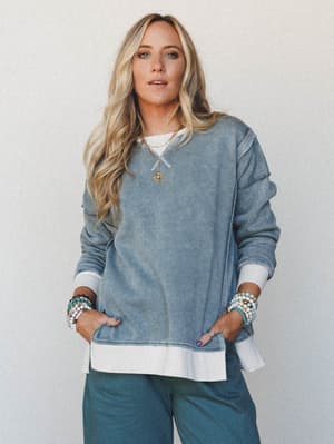 A relaxed, lived-in sweatshirt in washed ash jade layers effortlessly over a white tee, styled with wide-leg pants and stacked beaded bracelets — the kind of outfit that looks intentional without trying.