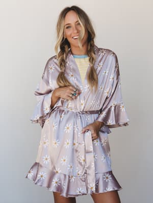 A satin daisy-print robe styled open over a striped tee — belted at the waist with ruffle trim at the hem and sleeves, giving it that 'I look this good on a slow morning' energy.