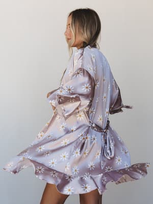 A model twirls in a satin daisy-print robe, the skirt caught mid-spin against a soft neutral backdrop — playful, dreamy, and a little bit magic.