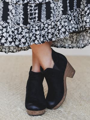 A close-up of black suede block-heel booties paired with a flowy black-and-white floral midi skirt with a lace hem — the kind of pairing that feels effortless but totally intentional.