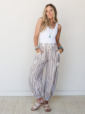 Relaxed striped jogger pants in a warm sandy tone styled with a white textured tank, stacked boho bracelets, and a turquoise pendant necklace — the kind of outfit that works equally well for a beach boardwalk or a slow Saturday morning.
