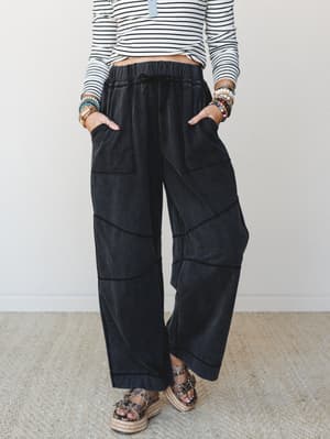Wide-leg ash black pants with geometric seam detailing styled with a striped crop top, stacked bracelets, and platform espadrille sandals — the kind of outfit that looks effortless but definitely had thought behind it.