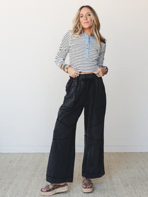 A relaxed full-body model shot pairing wide-leg ash black pants with seam detailing against a cropped striped henley — effortlessly put-together with a lived-in, casual-cool energy.