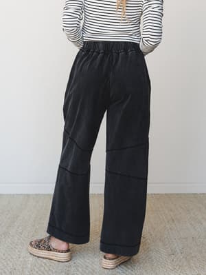 A back-view shot of wide-leg ash black pants with paneled seam detailing and an elastic waistband, styled with a striped long-sleeve top and leopard print platform espadrilles for a laid-back, put-together feel.