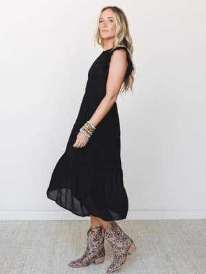 A black tiered maxi dress with flutter sleeves and smocked bodice, styled with leopard print western booties and a stack of colorful beaded bracelets — the kind of outfit that works as hard at brunch as it does at a concert.