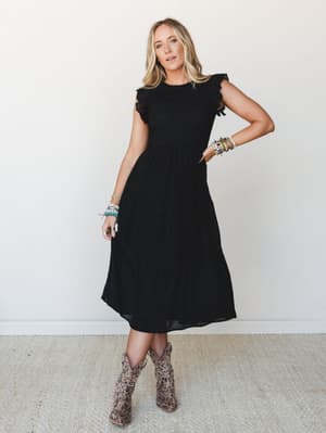 A black midi dress with flutter sleeves and a smocked bodice, styled with leopard print cowboy boots and stacked beaded bracelets against a clean studio wall — the kind of outfit that works for a date night and a country concert equally well.