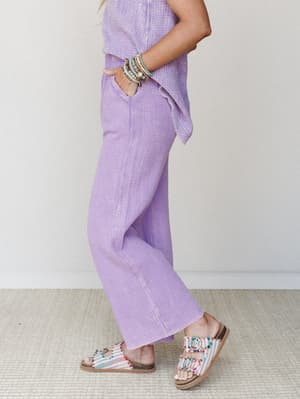 A side-profile shot of a matching lavender gauze set — relaxed wide-leg pants with a flowy top — styled with beaded sandals and a stacked bracelet stack that makes the whole look feel like a really good Saturday.