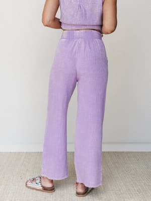 A back-view shot of wide-leg lavender pants in a textured gauze-like fabric, styled with a matching cropped top and floral sandals against a soft neutral studio backdrop — easy, put-together, and effortlessly relaxed.
