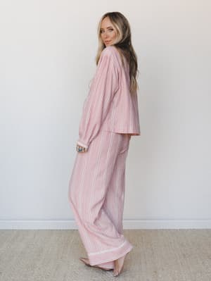 A relaxed two-piece pajama set in a pink and taupe plaid-stripe mix, styled on a model glancing back over her shoulder — the kind of set that blurs the line between staying in and looking put-together.