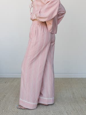 A side-angle shot of a matching striped set — wide-leg pants with a delicate crochet hem trim paired with a knotted crop top in the same print, giving off easy, relaxed energy against a soft neutral backdrop.
