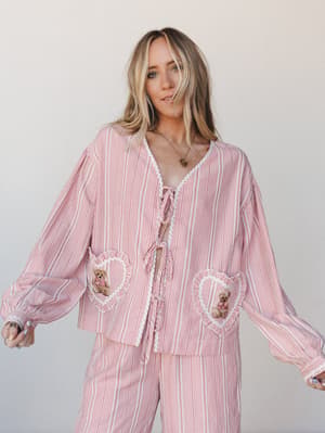 A relaxed matching set in a rosy pink gingham check, styled with playful heart-shaped pockets trimmed in white lace and tiny embroidered teddy bear patches — cozy and nostalgic with just enough whimsy to make it feel intentional.