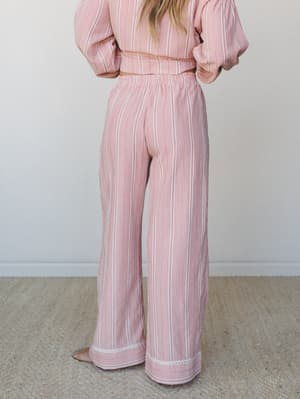 A back-view shot of a matching wide-leg pant and cropped top set in a soft pink and red woven stripe, styled casually indoors with a relaxed, easy-morning feel.