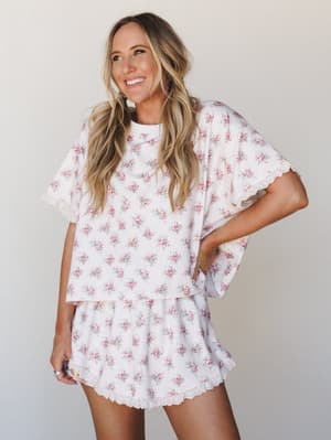 A matching floral short set with lace trim edges worn by a smiling model against a soft neutral backdrop — the kind of set that blurs the line between pajamas and something you'd actually wear out for coffee.