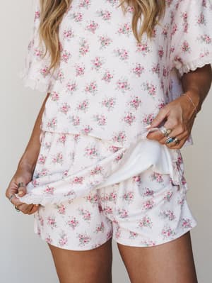 A floral waffle-knit matching set — short sleeve top and mini shorts in cream with scattered pink roses — styled with stacked silver and turquoise rings for that effortless, lived-in softness.