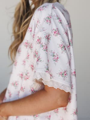 A close-up detail shot of a floral top with a waffle-knit texture, capturing the eyelet lace trim at the sleeve hem — soft, romantic, and the kind of thing you'd want to wake up in.