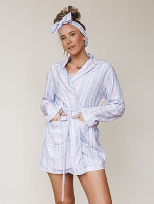 A model wears a floral stripe robe set in soft periwinkle and pink, styled with a matching bow headband — the kind of morning look that makes you want to stay in bed a little longer.
