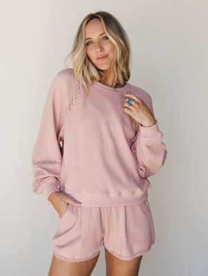 A matching waffle-knit pullover and shorts set in soft dusty pink, styled with silver rings and a turquoise stone — the kind of set that blurs the line between staying in and stepping out.