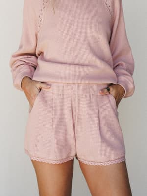 A blush pink waffle-knit matching set shot up close — the lace-trim shorts and long-sleeve top feel like the kind of cozy you actually want to be seen in.