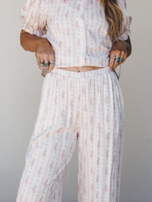 A matching floral two-piece set — cropped puff-sleeve top and wide-leg pants — in a soft pink floral stripe, styled with stacked silver and turquoise rings for that effortless, 'wore this all day and have no regrets' energy.