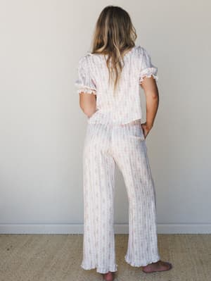 A matching floral print pajama set shot from the back — the soft pink-on-cream print, ruffle-trimmed sleeves, and wide-leg pants give it that dreamy, just-woke-up-and-still-look-cute energy.