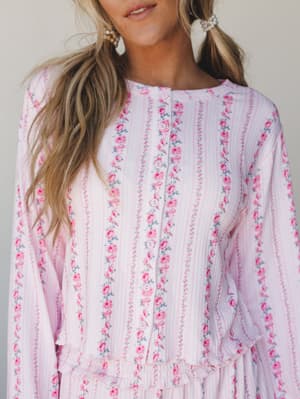 A close-up of a soft pink floral top with vertical stripe detailing and button-front closure — the kind of piece that blurs the line between getting dressed and staying cozy, in the best way.