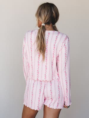 Shot from the back, a model wears a matching ribbed floral long-sleeve top and shorts set in soft pink — the kind of set that blurs the line between pajamas and something you'd actually wear to brunch.