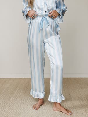 A soft satin stripe pajama set in powder blue and white, styled with stacked silver and turquoise rings — the kind of set that makes staying in feel like an actual event.