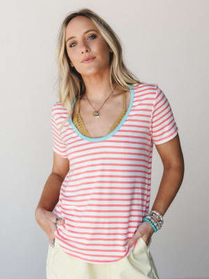 A relaxed coral stripe tee with a playful turquoise scoop neck trim, styled with layered boho jewelry and pale yellow pants — the kind of effortless summer outfit that looks like you tried just the right amount.