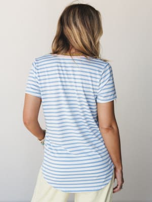 A back-view shot of a relaxed striped tee in sky blue and white, paired with soft cream pants — the kind of easy, put-together look that works just as hard on a coffee run as it does at the farmers market.