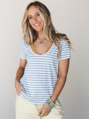 A relaxed striped scoop-neck tee in sky blue and white, styled with soft yellow pants and layered boho jewelry — the kind of easy, happy outfit that works for basically everything.