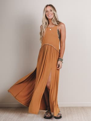 Woman wearing a long mustard yellow dress with a slit, standing against a plain background.