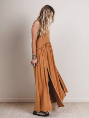 Woman wearing a long brown dress against a plain wall.