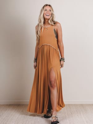 Woman wearing a long mustard yellow dress with a slit, standing against a plain background.