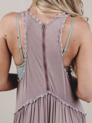 Back view of a woman wearing a sleeveless dress with lace details on a plain background