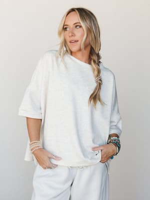 An oversized heather vanilla tee styled with matching wide-leg sweatpants and stacked boho bracelets — the kind of effortless monochromatic moment that somehow looks intentional.