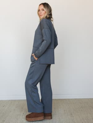 A matching two-piece set in heathered charcoal — relaxed open-front blazer and wide-leg pants styled with cozy brown platform boots, shot in profile against a clean white studio wall with an easy, lived-in confidence.