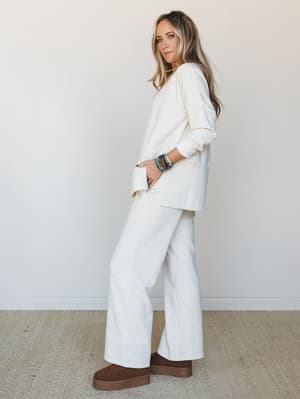 A matching heather vanilla set — relaxed long-sleeve top and wide-leg pants in a soft knit fabric — styled with chunky brown platform boots and a stack of colorful beaded bracelets for a lived-in, effortlessly cozy look.