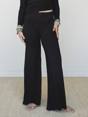 A relaxed wide-leg pant with a fold-over waistband styled with a black ribbed long-sleeve top, beaded bracelets, and nude sandals — the kind of effortless all-black look that feels intentional without trying too hard.