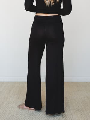 A back-view shot of wide-leg black pants with a fold-over waistband, paired with a black ribbed long-sleeve crop top and studded sandals — relaxed and put-together at the same time.