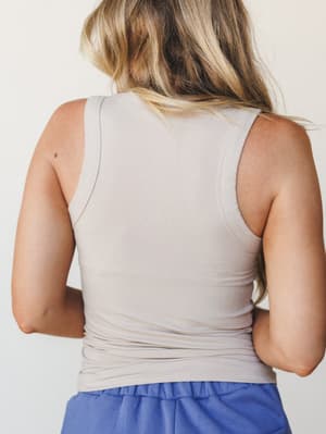 A back-view shot of a ribbed fitted tank in soft light mocha, paired with periwinkle blue bottoms — simple, clean, and the kind of top that goes with everything without trying too hard.
