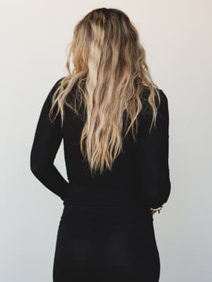 A back-facing studio shot of a model in an all-black ribbed long sleeve top and matching skirt — simple, relaxed, and the kind of outfit that does the heavy lifting without trying too hard.