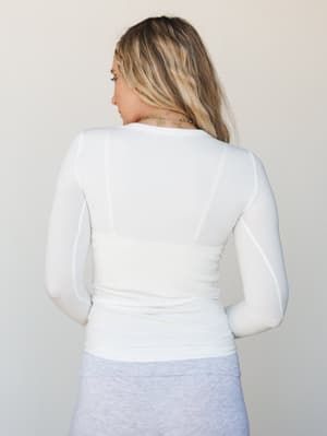 A back-view shot of a fitted white ribbed long sleeve top, styled with a heather grey skirt — clean, effortless, and the kind of layering piece that quietly holds an entire outfit together.