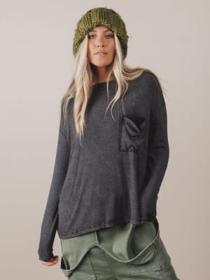 Woman wearing a dark gray long-sleeve top and green pants with a green knit hat on a beige background