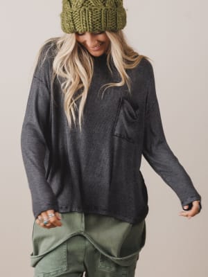 Person wearing a dark gray oversized sweatshirt and green knit beanie with a neutral background