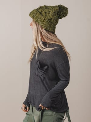 Person wearing a green knitted beanie and dark gray long-sleeve shirt on a beige background