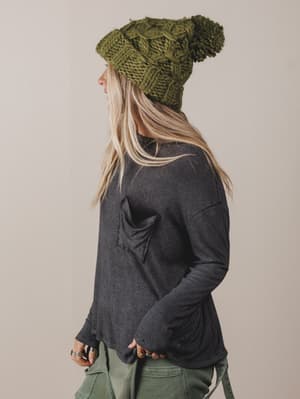 Person wearing a green knitted beanie and dark gray long-sleeve shirt on a beige background